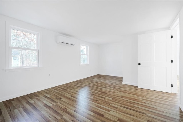 empty room featuring hardwood / wood-style flooring, a wall unit AC, and plenty of natural light