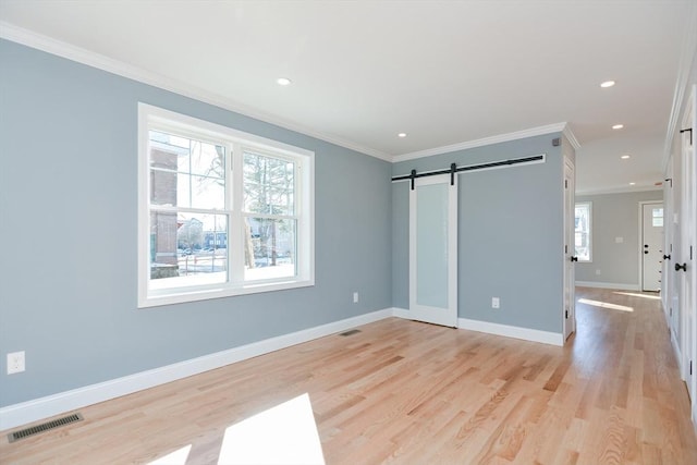 unfurnished bedroom featuring multiple windows, crown molding, a barn door, and light wood-type flooring