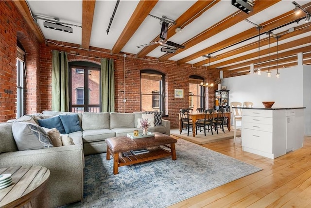 living room featuring beam ceiling, light wood-type flooring, ceiling fan with notable chandelier, and brick wall