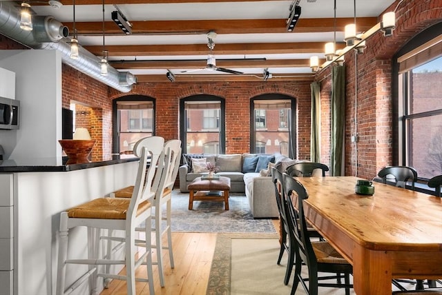 dining room with beamed ceiling, brick wall, and light hardwood / wood-style flooring