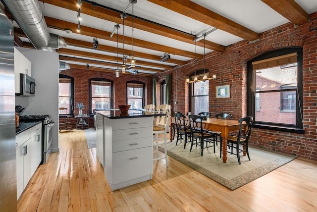 kitchen featuring decorative light fixtures, stainless steel appliances, light hardwood / wood-style floors, and brick wall