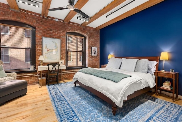 bedroom featuring beamed ceiling, brick wall, hardwood / wood-style flooring, and ceiling fan