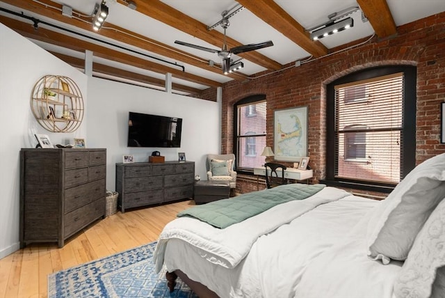 bedroom with light wood-type flooring, track lighting, beamed ceiling, and brick wall