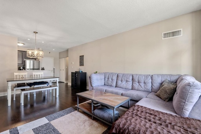 living area with a textured ceiling, a chandelier, baseboards, dark wood-type flooring, and visible vents