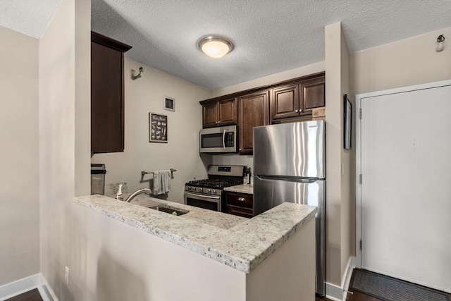 kitchen with dark brown cabinetry, a textured ceiling, appliances with stainless steel finishes, a sink, and a peninsula
