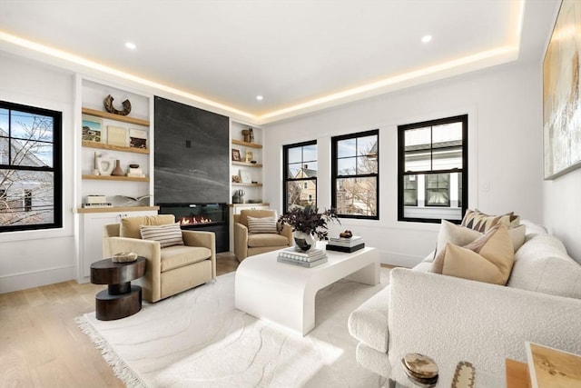 living room featuring a large fireplace, light wood-type flooring, a raised ceiling, and built in features