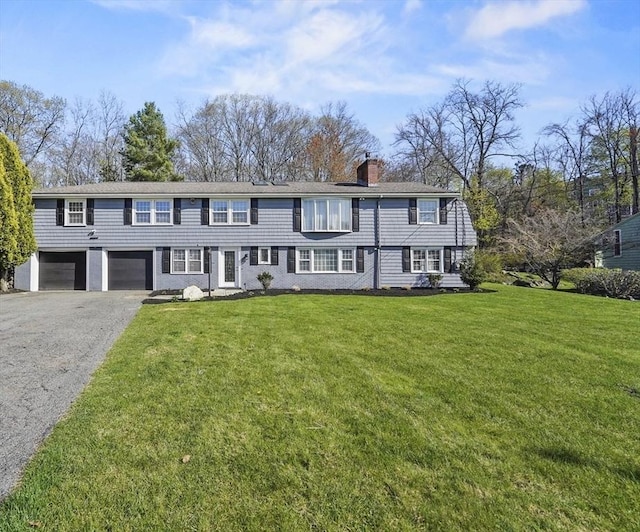 view of front facade featuring a chimney, an attached garage, a front yard, and aphalt driveway