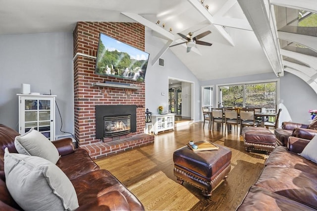 living area with ceiling fan, visible vents, a brick fireplace, beam ceiling, and wood finished floors