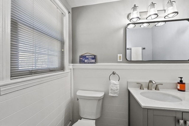 half bath featuring vanity, a wainscoted wall, and toilet