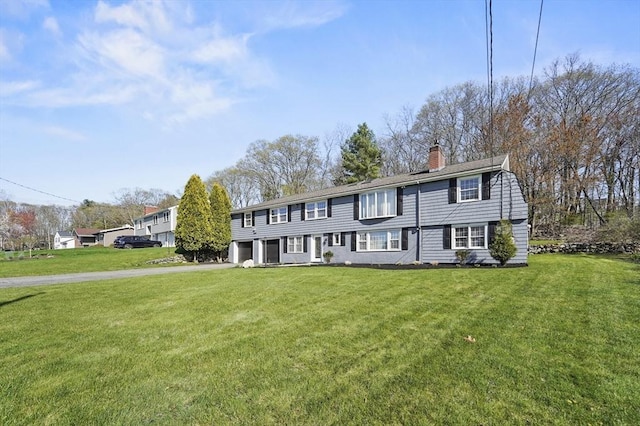 colonial inspired home featuring an attached garage, driveway, a chimney, and a front yard