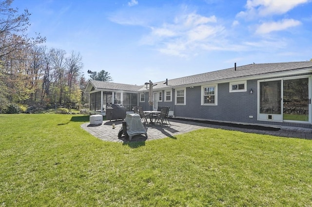 rear view of house with a sunroom, a lawn, brick siding, and a patio