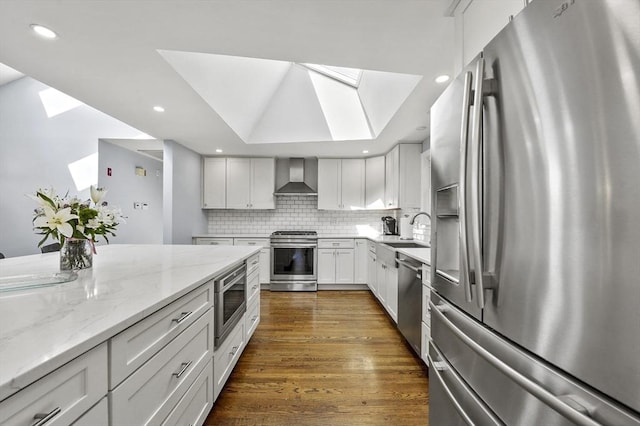 kitchen featuring decorative backsplash, wall chimney exhaust hood, light stone counters, a skylight, and stainless steel appliances