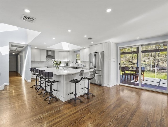 kitchen featuring visible vents, a skylight, stainless steel fridge with ice dispenser, dark wood-style floors, and wall chimney exhaust hood