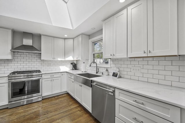 kitchen featuring decorative backsplash, appliances with stainless steel finishes, a sink, light stone counters, and wall chimney exhaust hood