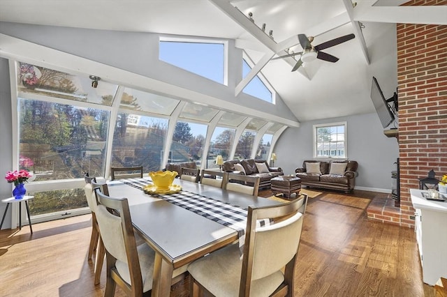 dining room with a brick fireplace, high vaulted ceiling, a ceiling fan, baseboards, and wood finished floors