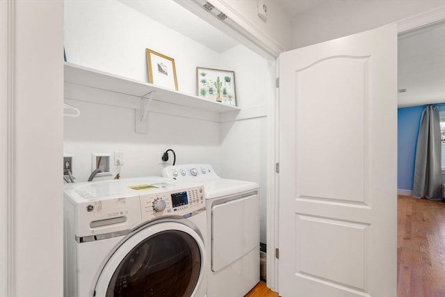 laundry room with washing machine and clothes dryer and light hardwood / wood-style flooring