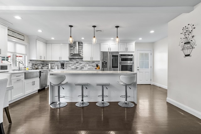 kitchen with wall chimney exhaust hood, a kitchen island, appliances with stainless steel finishes, and white cabinetry