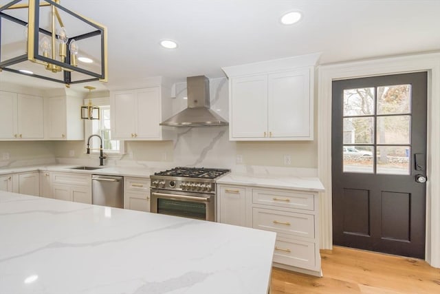 kitchen featuring white cabinetry, stainless steel appliances, wall chimney exhaust hood, and a sink