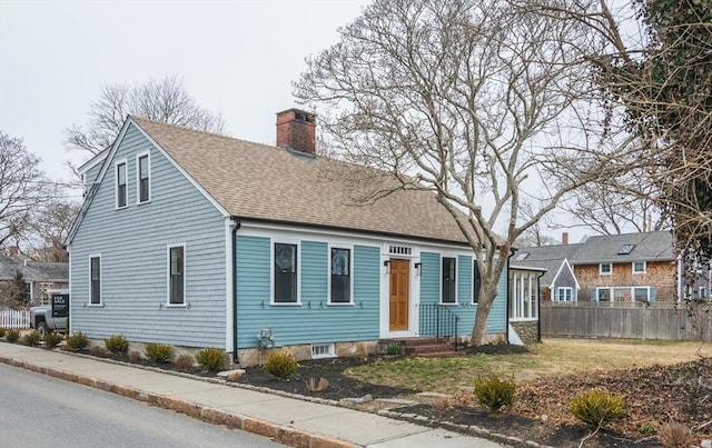 cape cod home with a chimney, roof with shingles, and fence