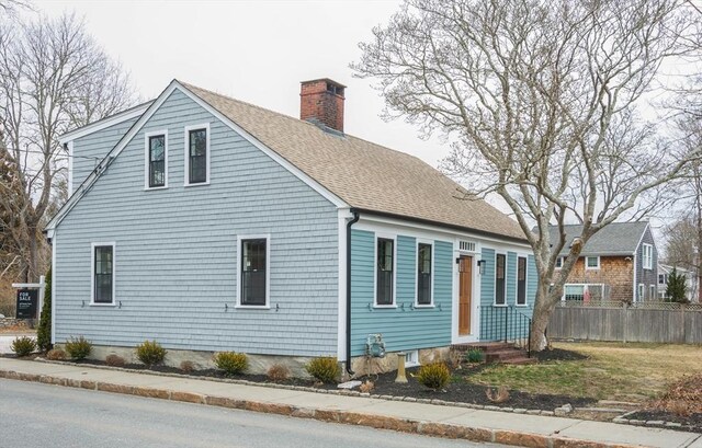 view of side of home featuring a shingled roof, a chimney, and fence