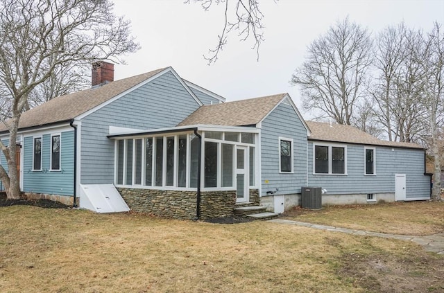 back of house featuring roof with shingles, a yard, a sunroom, a chimney, and central air condition unit