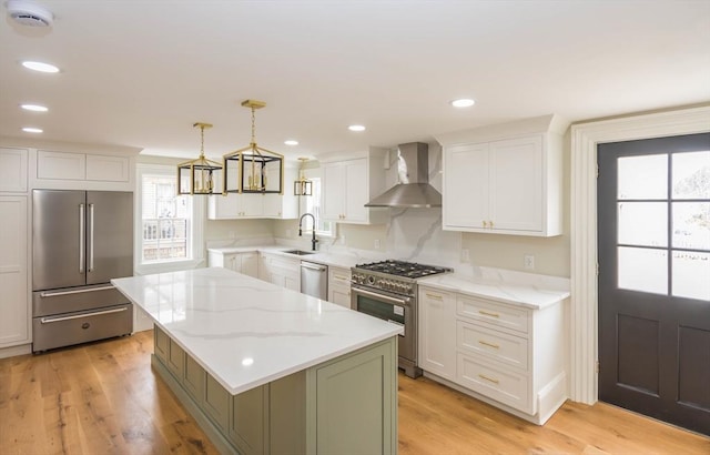 kitchen featuring high quality appliances, a sink, wall chimney range hood, a kitchen island, and light wood finished floors