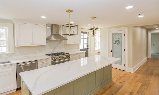 kitchen with stainless steel appliances, light wood finished floors, white cabinets, and wall chimney range hood