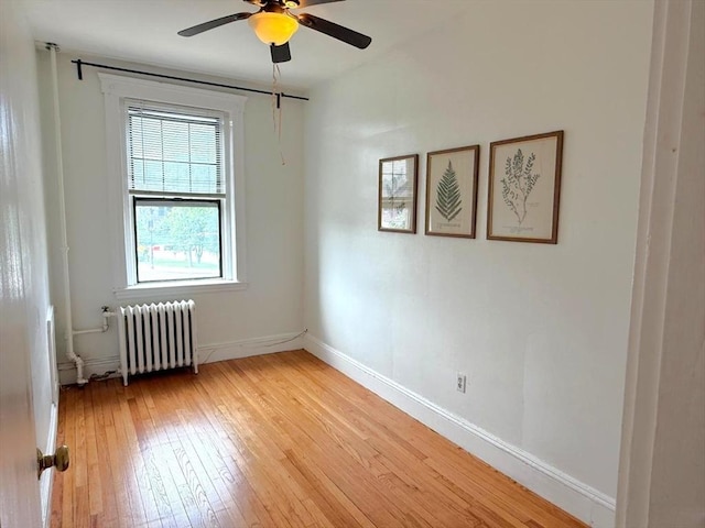 empty room with radiator heating unit, light wood-style floors, a ceiling fan, and baseboards