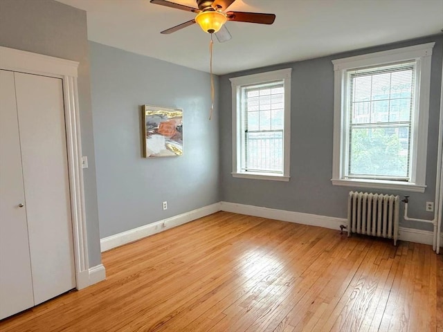 unfurnished bedroom featuring radiator, light wood-style floors, baseboards, and ceiling fan