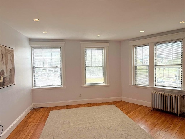 empty room with radiator, light wood-type flooring, recessed lighting, and baseboards