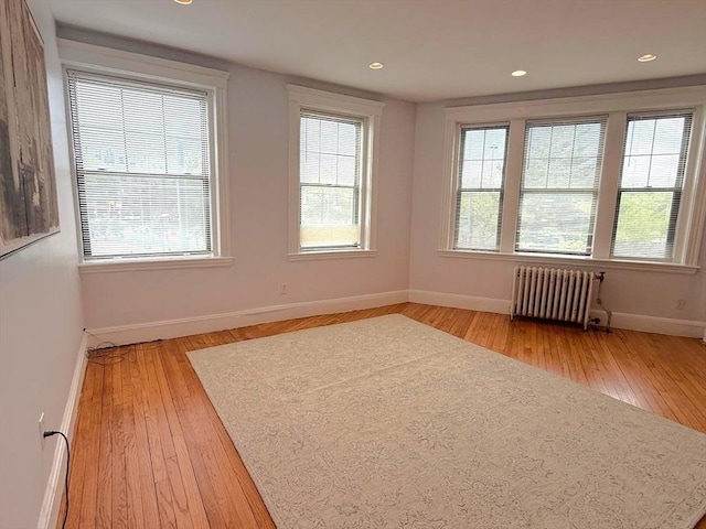empty room with radiator, light wood-style flooring, baseboards, and recessed lighting