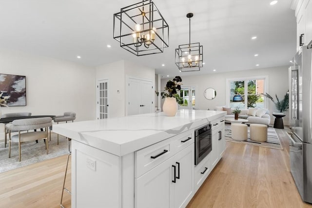 kitchen with stainless steel fridge, white cabinetry, and hanging light fixtures