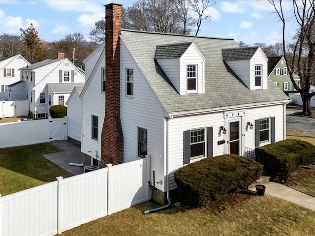 cape cod-style house featuring a front lawn, a gate, a fenced backyard, a shingled roof, and a chimney