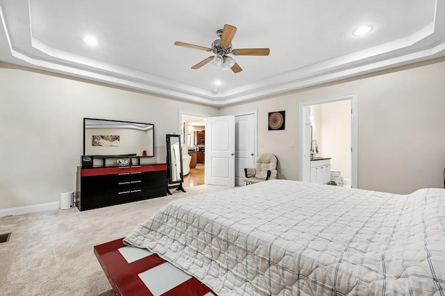 carpeted bedroom featuring a raised ceiling and ensuite bathroom