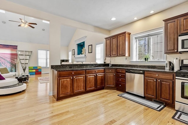 kitchen featuring appliances with stainless steel finishes, lofted ceiling, sink, dark stone counters, and light hardwood / wood-style flooring