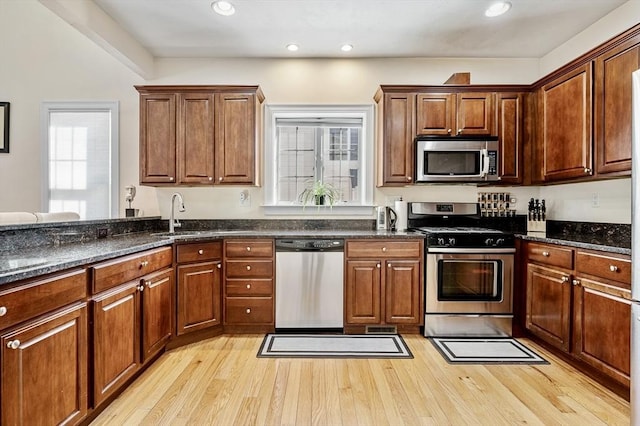 kitchen with dark stone countertops, sink, stainless steel appliances, and light wood-type flooring