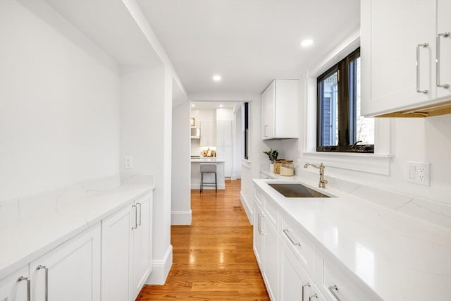 kitchen with light stone counters, sink, white cabinets, and light hardwood / wood-style floors