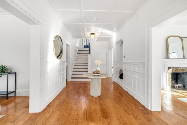 foyer entrance with wood-type flooring, a stone fireplace, and coffered ceiling