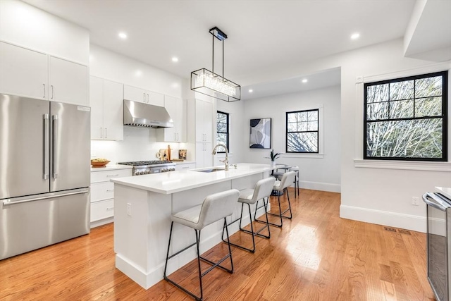 kitchen with stainless steel refrigerator, white cabinetry, a center island with sink, and hanging light fixtures