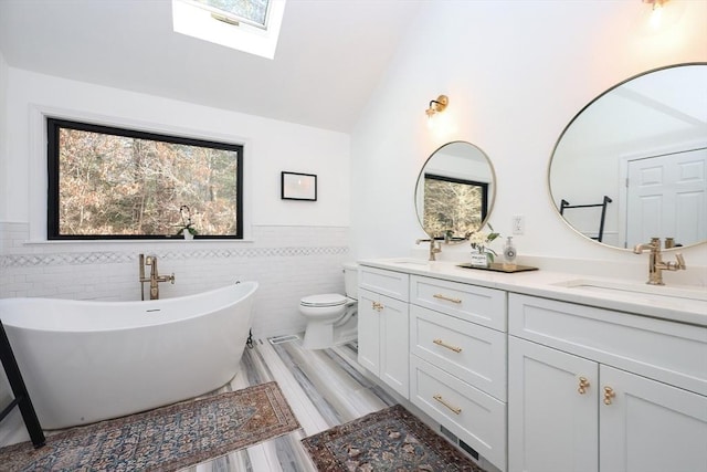 bathroom with tile walls, vaulted ceiling with skylight, vanity, a tub to relax in, and toilet