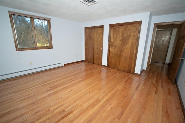 unfurnished bedroom featuring a baseboard radiator, two closets, and light wood-type flooring