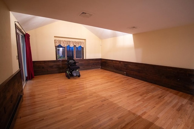 spare room with wood walls, light hardwood / wood-style floors, and vaulted ceiling