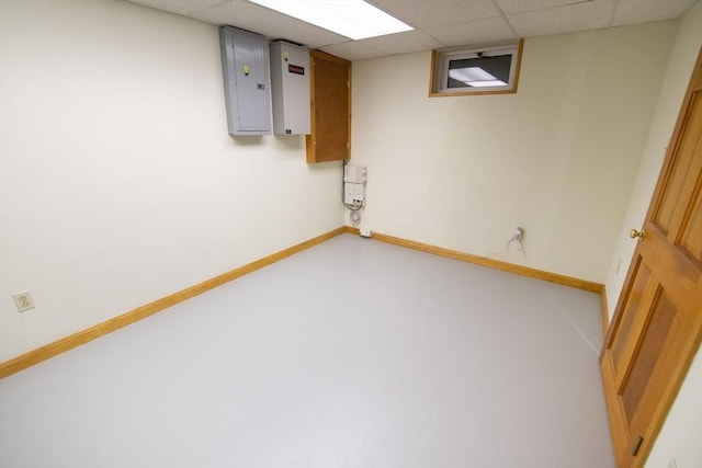 basement with a paneled ceiling and electric panel