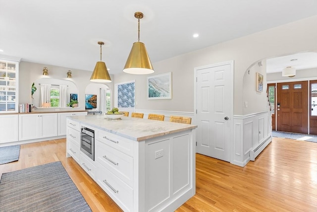 38 Thoreau Cir, Beverly, MA 01915 - kitchen with arched walkways, a baseboard radiator, light wood-type flooring, stainless steel microwave, and white cabinets