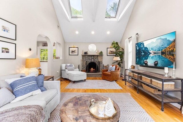 38 Thoreau Cir, Beverly, MA 01915 - living room with high vaulted ceiling, arched walkways, a stone fireplace, light wood-style flooring, and a skylight