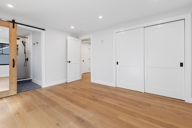 unfurnished bedroom featuring a barn door, light hardwood / wood-style flooring, and a closet