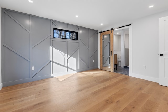 basement with a barn door and light hardwood / wood-style floors