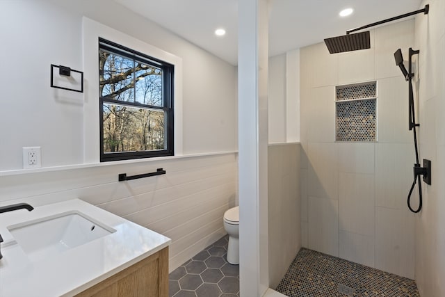 bathroom featuring a tile shower, tile patterned flooring, toilet, vanity, and tile walls