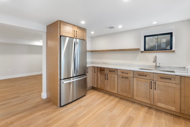 kitchen featuring stainless steel fridge, sink, light hardwood / wood-style floors, and light stone counters