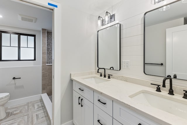 bathroom with a tile shower, vanity, and toilet